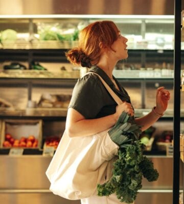 Photo shows a young woman with green leafy vegetables in her bag shopping at a supermarket