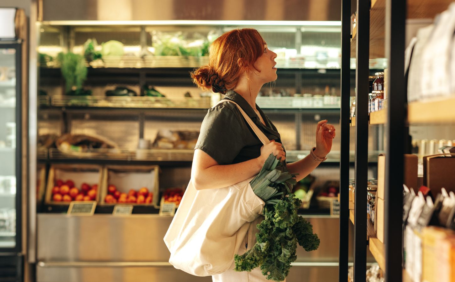 Photo shows a young woman with green leafy vegetables in her bag shopping at a supermarket