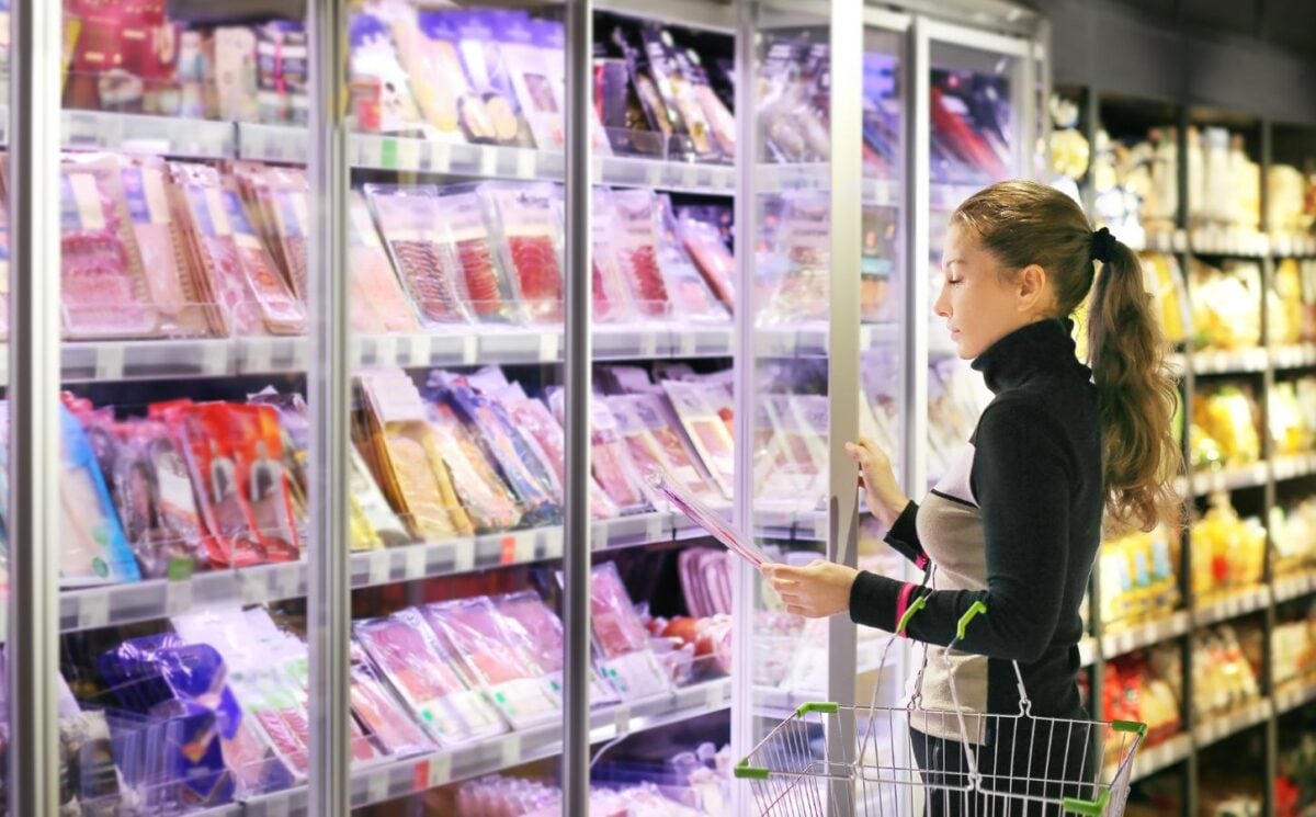 Photo shows a young woman looking at the cured and pre-cooked meat section in a supermarket