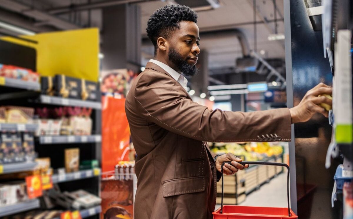 Photo shows a shopper in the supermarket, holding a basket and about to take an item off the shelf