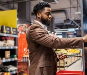 Photo shows a shopper in the supermarket, holding a basket and about to take an item off the shelf