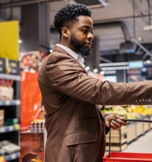 Photo shows a shopper in the supermarket, holding a basket and about to take an item off the shelf