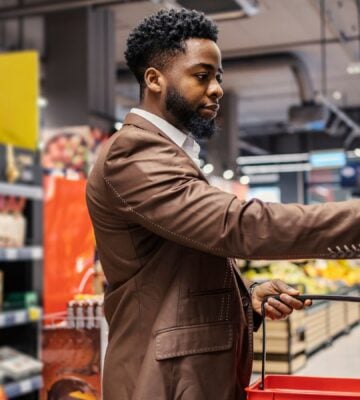 Photo shows a shopper in the supermarket, holding a basket and about to take an item off the shelf