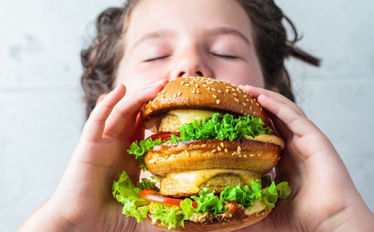 Photo shows a young boy about to take a bit out of a large vegan burger