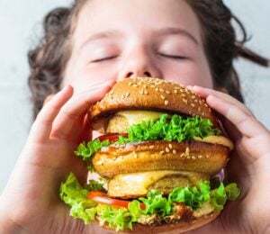 Photo shows a young boy about to take a bit out of a large vegan burger