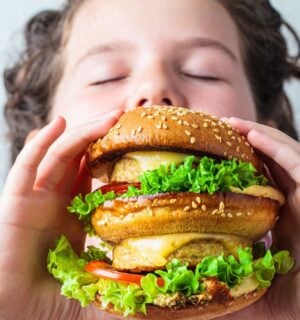 Photo shows a young boy about to take a bit out of a large vegan burger