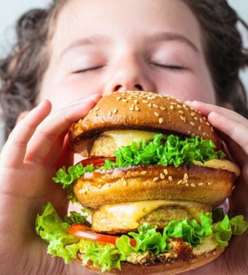 Photo shows a young boy about to take a bit out of a large vegan burger