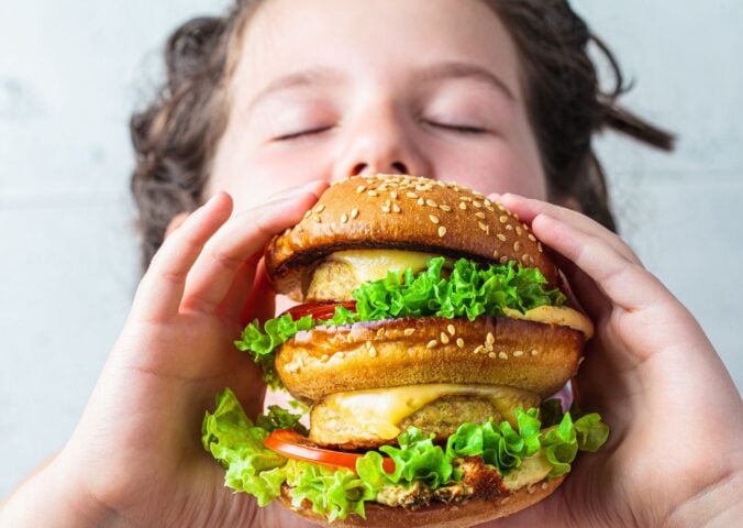 Photo shows a young boy about to take a bit out of a large vegan burger