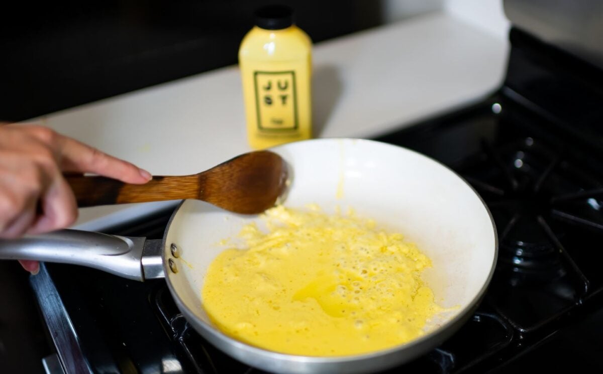 Photo shows someone cooking a pan of Eat Just's vegan egg product, "Just Egg," with the packaging visible in the background