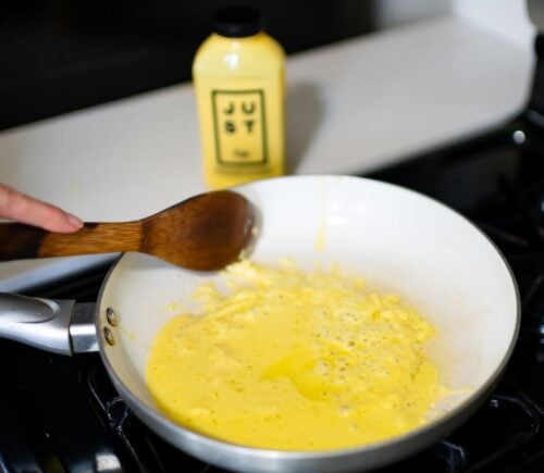 Photo shows someone cooking a pan of Eat Just's vegan egg product, "Just Egg," with the packaging visible in the background