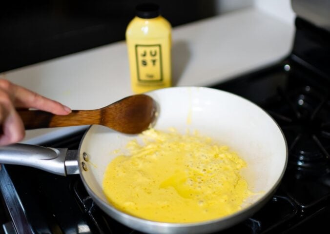 Photo shows someone cooking a pan of Eat Just's vegan egg product, "Just Egg," with the packaging visible in the background