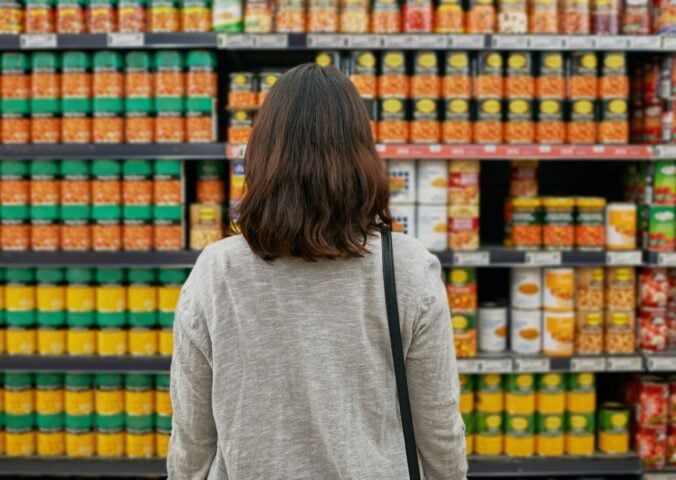A woman looking at tins of beans at a supermarket