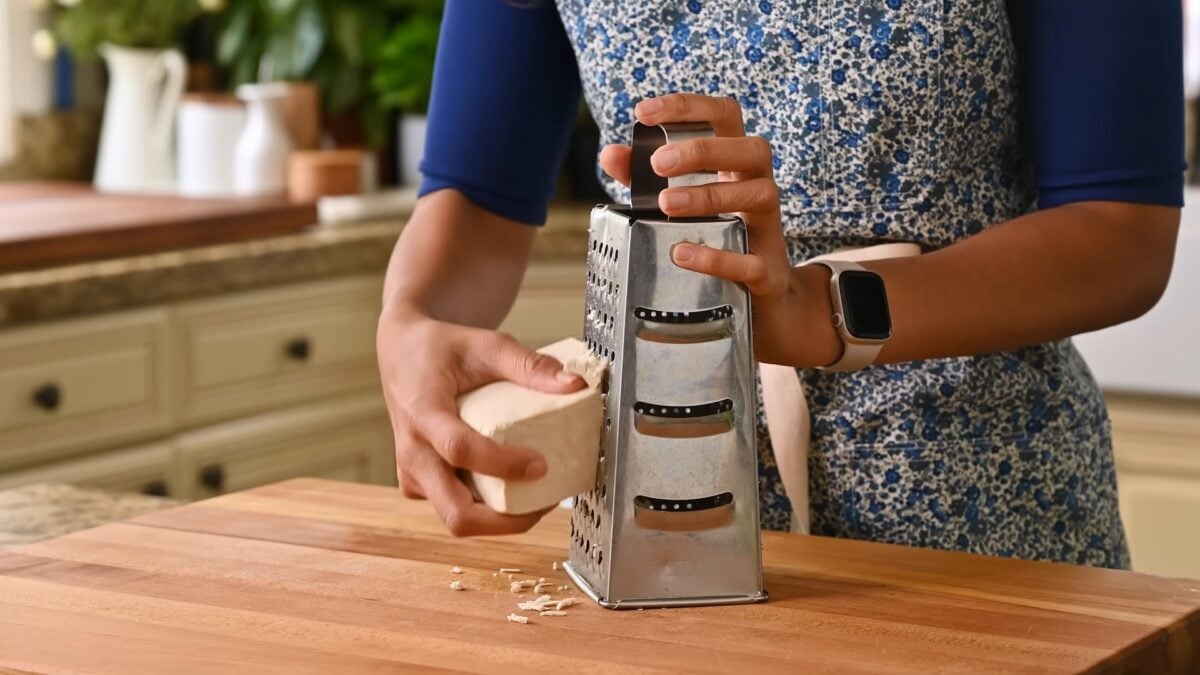 Nisha Vora stands in her kitchen grating a block of tofu to make her grated tofu recipe.