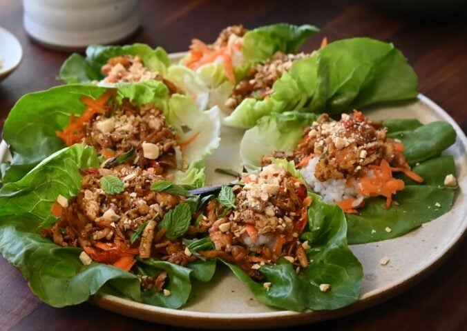 A plate of fresh lettuce wraps filled with a block of tofu, sushi rice, shredded carrots, herbs, and crushed peanuts