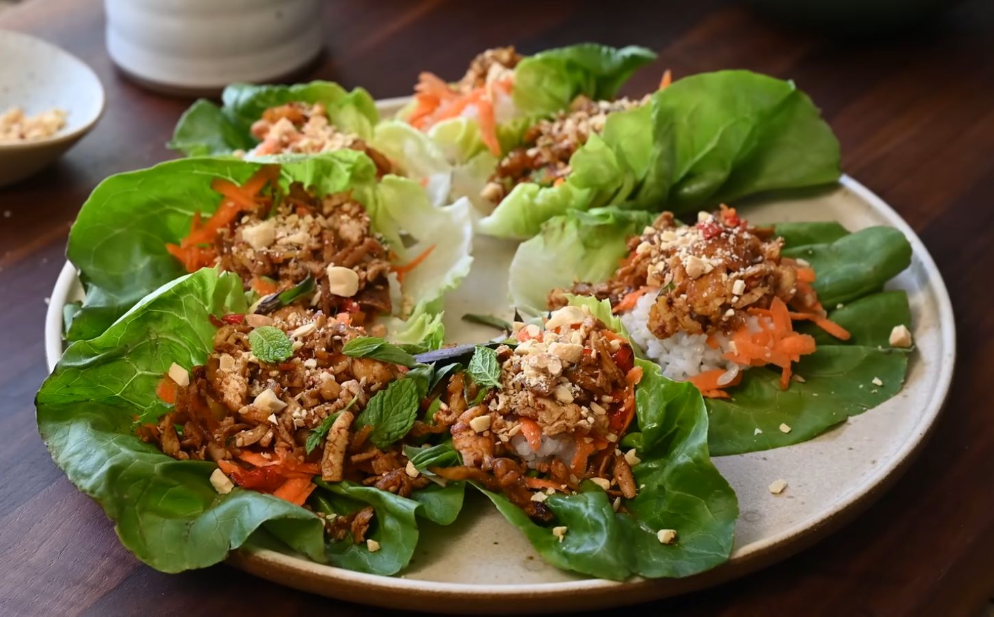 A plate of fresh lettuce wraps filled with a block of tofu, sushi rice, shredded carrots, herbs, and crushed peanuts