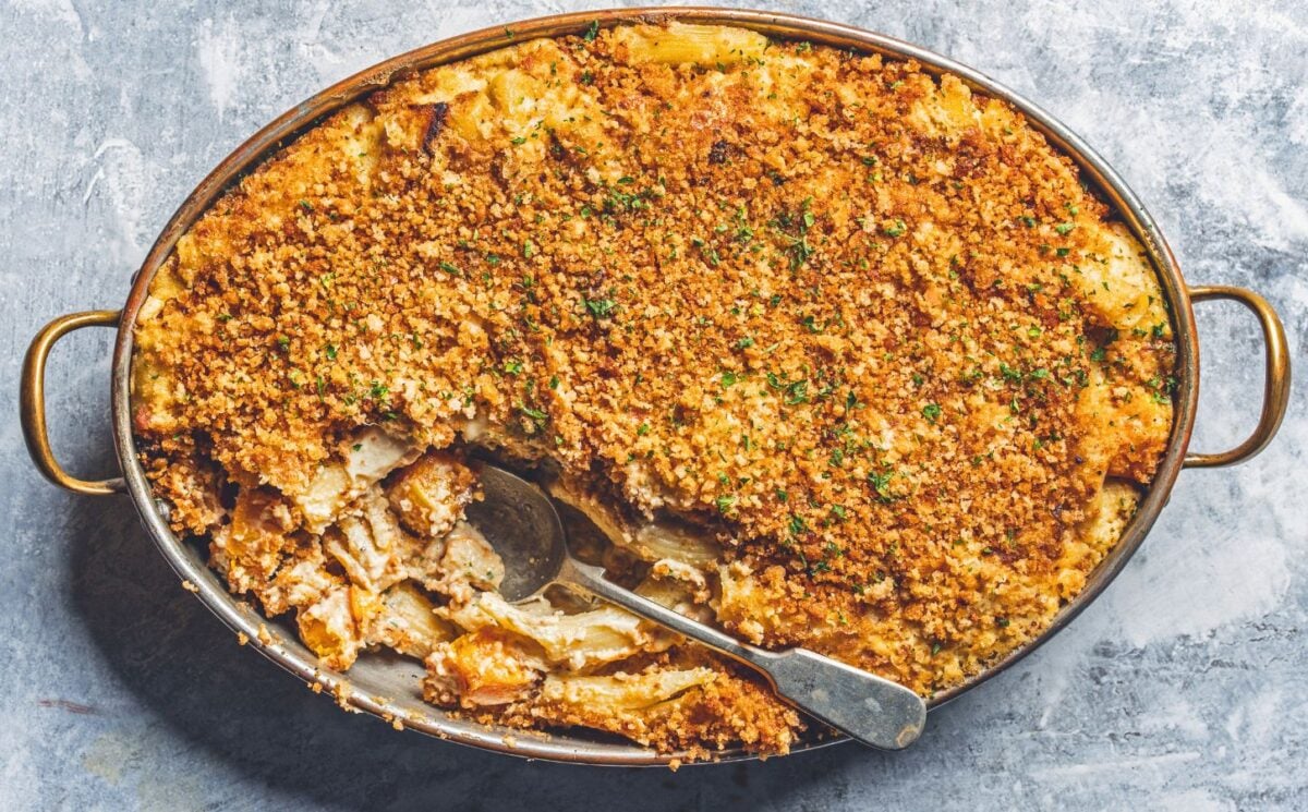 a dish of vegan baked ziti alfredo made with ziti pasta, vegan alfredo sauce, asparagus, mozzarella, and breadcrumbs