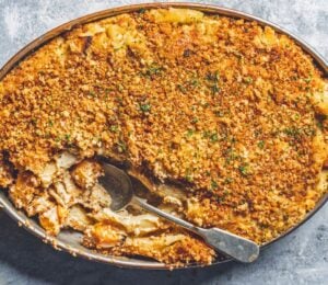 a dish of vegan baked ziti alfredo made with ziti pasta, vegan alfredo sauce, asparagus, mozzarella, and breadcrumbs