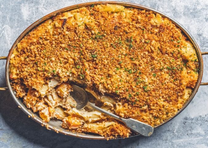 a dish of vegan baked ziti alfredo made with ziti pasta, vegan alfredo sauce, asparagus, mozzarella, and breadcrumbs
