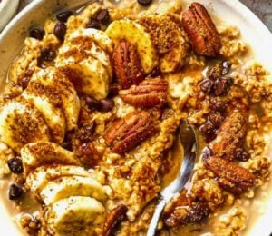 a bowl of banana, walnut and chocolate porridge with nutty drizzle and vegan protein powder