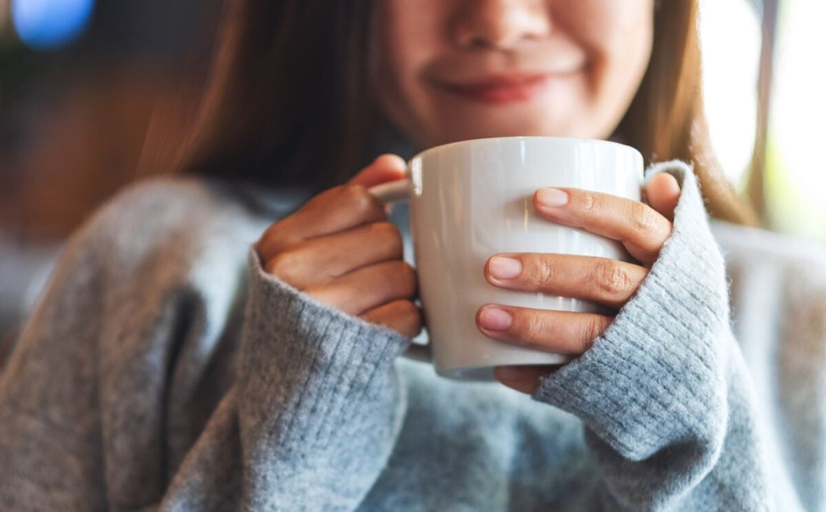 Photo shows a young woman holding a mug of coffee and smiling. A new study indicates that drinking a cup of coffee first thing in the morning really does make you happy