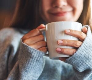 Photo shows a young woman holding a mug of coffee and smiling. A new study indicates that drinking a cup of coffee first thing in the morning really does make you happy