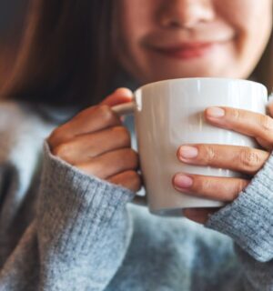 Photo shows a young woman holding a mug of coffee and smiling. A new study indicates that drinking a cup of coffee first thing in the morning really does make you happy