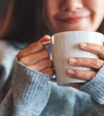 Photo shows a young woman holding a mug of coffee and smiling. A new study indicates that drinking a cup of coffee first thing in the morning really does make you happy