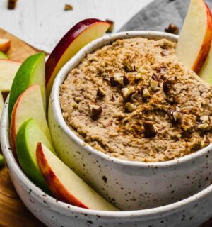 a bowl of creamy maple and toasted pecan dip with sliced apples on the side