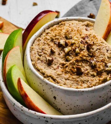 a bowl of creamy maple and toasted pecan dip with sliced apples on the side