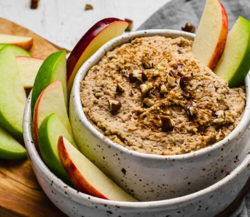 a bowl of creamy maple and toasted pecan dip with sliced apples on the side