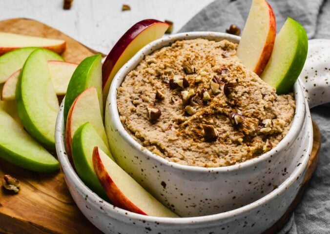 a bowl of creamy maple and toasted pecan dip with sliced apples on the side