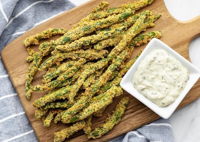 A wooden chopping board covered in oil-free green bean fries for green bean recipes