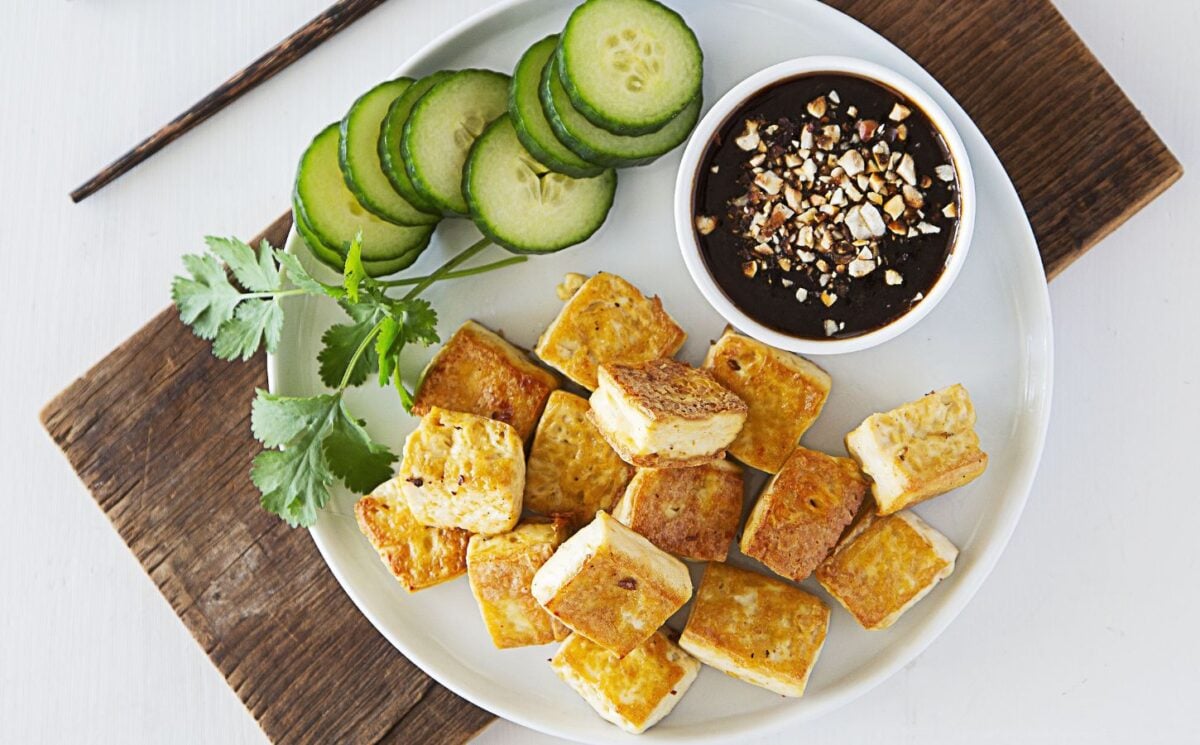 a plate of crispy tofu dipped in sweet and sour sauce with a side of cucumber