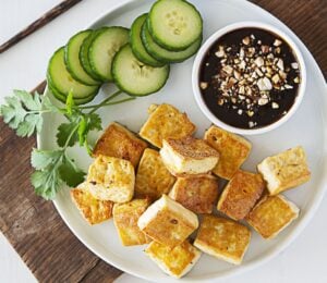 a plate of crispy tofu dipped in sweet and sour sauce with a side of cucumber
