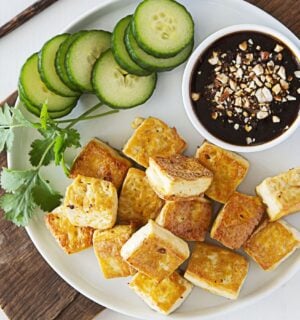 a plate of crispy tofu dipped in sweet and sour sauce with a side of cucumber