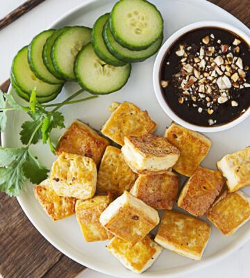 a plate of crispy tofu dipped in sweet and sour sauce with a side of cucumber