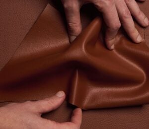 Photo shows someone's hands as they spread out a piece of "ELEVATE," a plant-based leather alternative for car interiors produced by UNCAGED and Hyundai