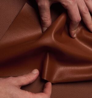 Photo shows someone's hands as they spread out a piece of "ELEVATE," a plant-based leather alternative for car interiors produced by UNCAGED and Hyundai