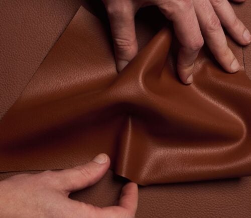 Photo shows someone's hands as they spread out a piece of "ELEVATE," a plant-based leather alternative for car interiors produced by UNCAGED and Hyundai