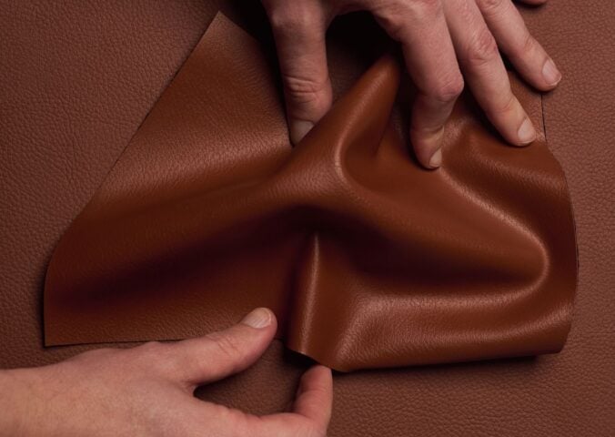Photo shows someone's hands as they spread out a piece of "ELEVATE," a plant-based leather alternative for car interiors produced by UNCAGED and Hyundai