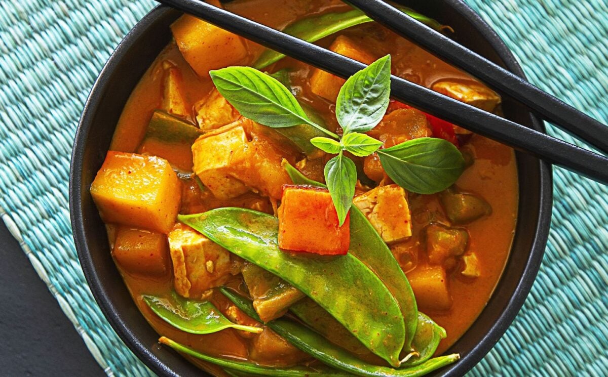 a bowl of mango red curry with mango pieces, tofu, and snow peas
