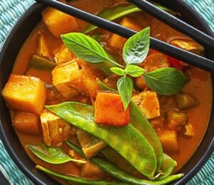 a bowl of mango red curry with mango pieces, tofu, and snow peas