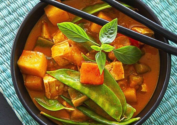 a bowl of mango red curry with mango pieces, tofu, and snow peas