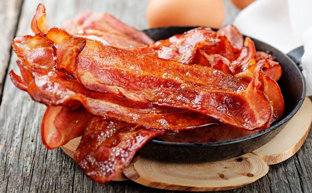 Photo shows a bowl of bacon next two whole eggs
