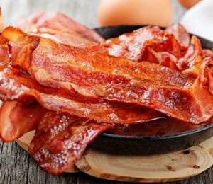 Photo shows a bowl of bacon next two whole eggs