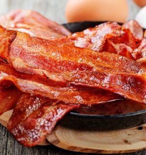 Photo shows a bowl of bacon next two whole eggs