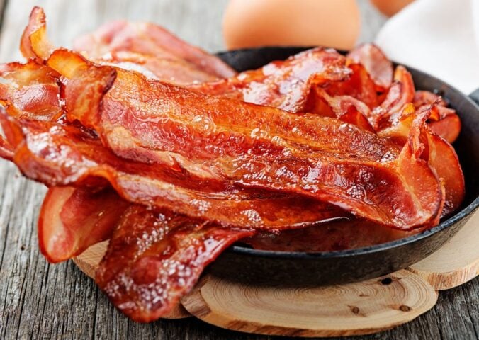 Photo shows a bowl of bacon next two whole eggs