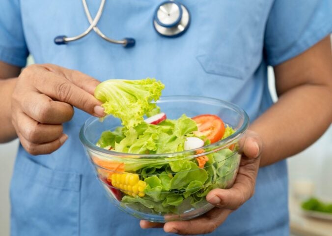 Plant-based diets are thought to cut disease risk, and the photo shows a Dr wearing scrubs and a stethoscope holding a glass bowl of salad