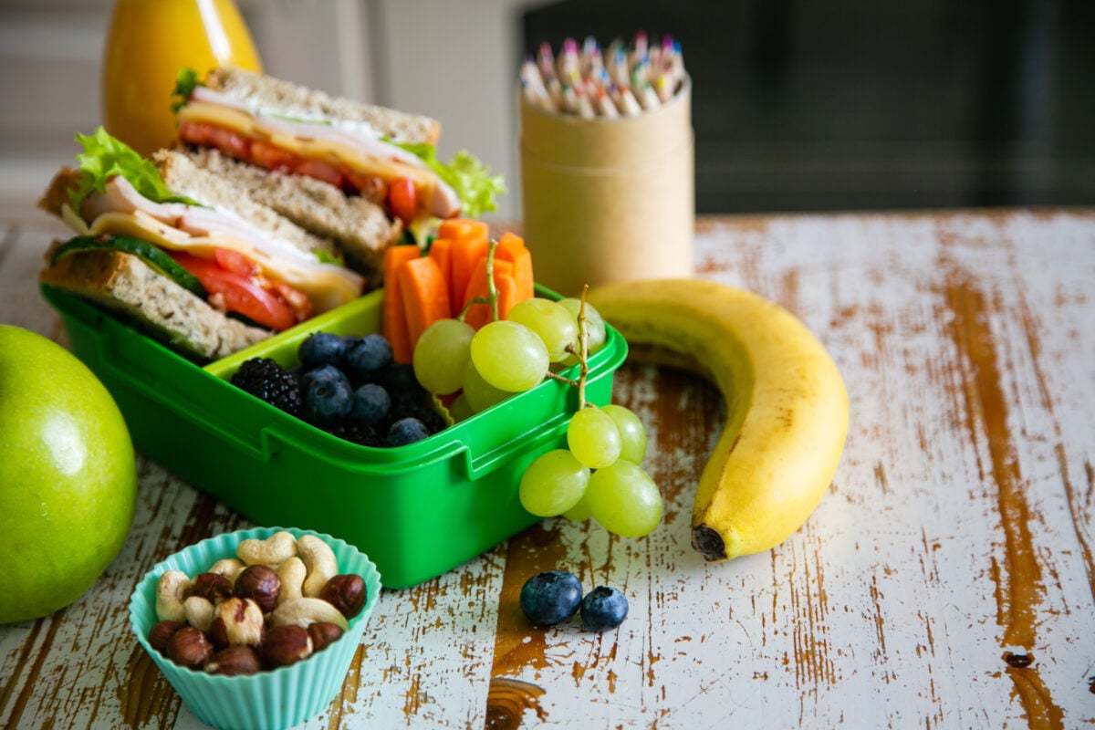 Photo shows a packed lunch for a school child featuring fruit, nuts, and a tomato and lettuce sandwich