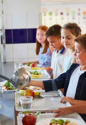 Nearly half of UK parents want more plant-based meals in schools. Photo shows a queue of school children loading their trays with fruit and vegetables